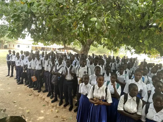 Secondary school assembly gathered outdoors under a large tree, The Gambia, 2022