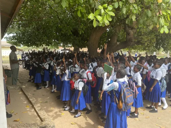 Secondary school assembly gathered outdoors under a large tree, The Gambia, 2022