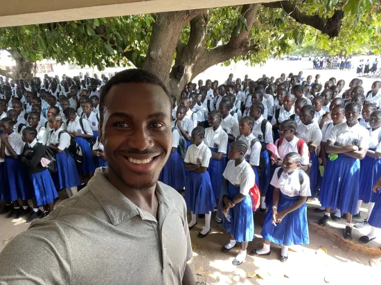 Secondary school assembly gathered outdoors under a large tree, The Gambia, 2022